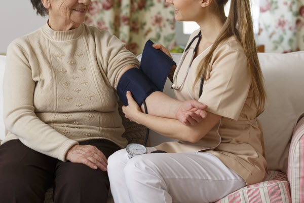 Examinierte Pflegefachkraft beim Blutdruck messen einer Seniorin