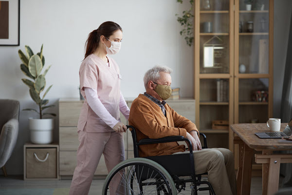 Pflegekraft mit Schutzmaske kümmert sich um Patient im Rollstuhl